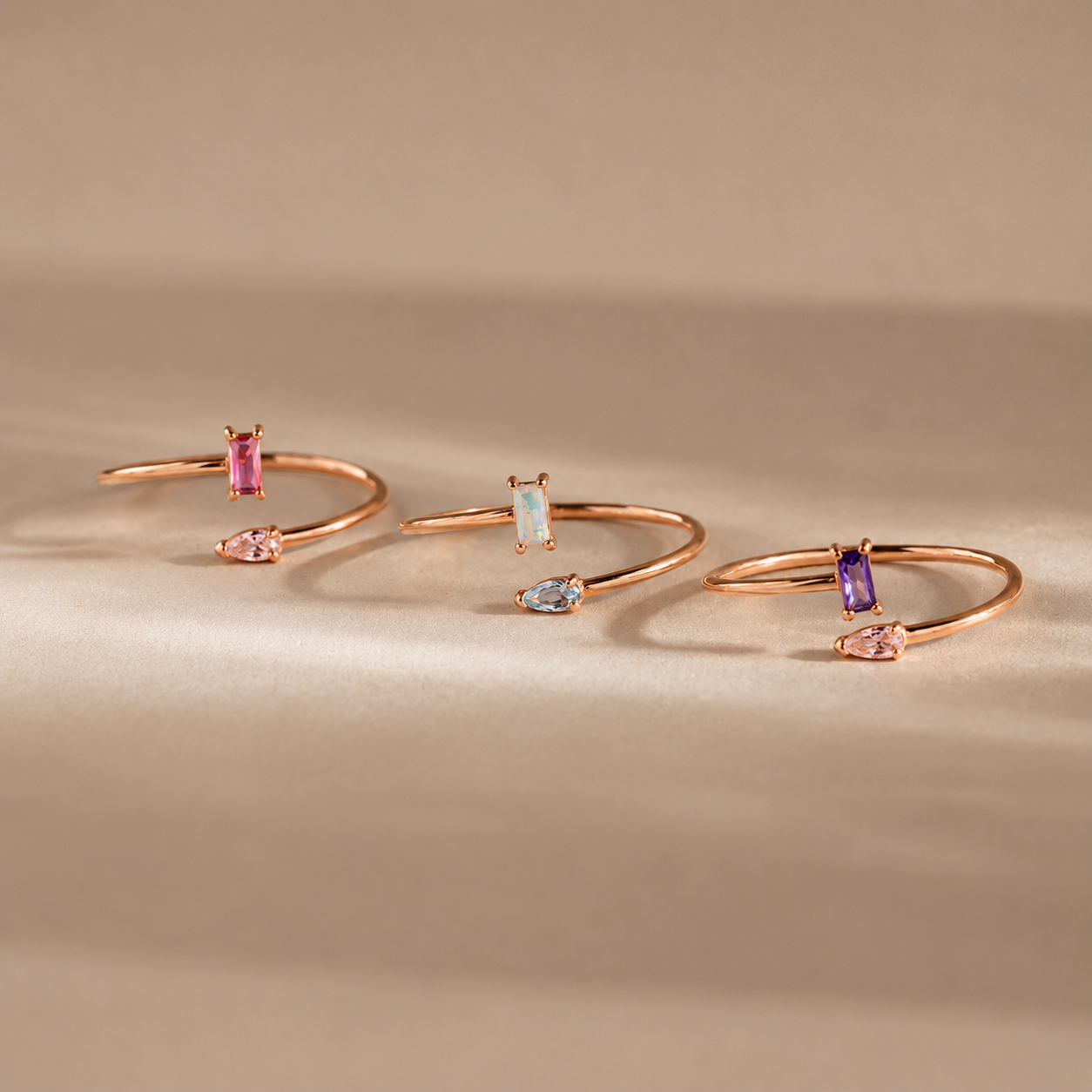 Three rose gold open rings with gemstones on a beige background